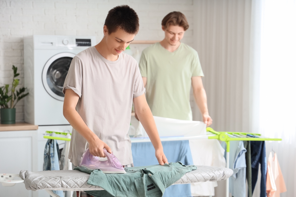 Male,Student,Ironing,Clothes,In,Dorm,Laundry,Room